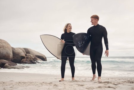 Foto de Nos acercamos un poco más a cada sesión de surf. una joven pareja en la playa con sus tablas de surf - Imagen libre de derechos