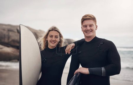 Téléchargez les photos : Surfer ensemble nous a rendus plus résilients en tant que couple. un jeune couple à la plage avec leurs planches de surf - en image libre de droit