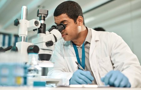 Photo for Its been a day full of tests. a young scientist writing notes while using a microscope in a lab - Royalty Free Image