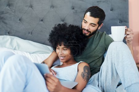 Téléchargez les photos : On peut regarder ensemble ? un jeune couple regardant quelque chose sur une tablette numérique tout en étant couché au lit - en image libre de droit