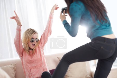 Foto de Mujeres locas amigas con una cámara fotográfica en felicidad juntas y siendo tontas en una sala de estar en casa. Diversión, gente y fotógrafo toman fotos de una mujer feliz celebrando. - Imagen libre de derechos