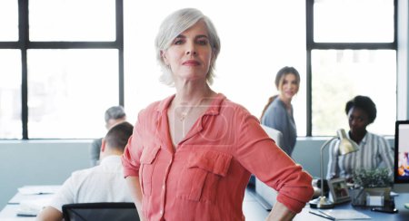 Photo for The right management can raise a teams performance. Portrait of a confident mature businesswoman working in a modern office with her colleagues in the background - Royalty Free Image
