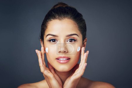 Photo for To achieve flawless skin, look after it. Studio shot of a beautiful young woman with moisturizer on her face while posing against a blue background - Royalty Free Image