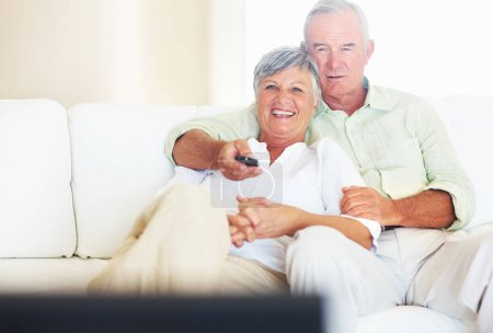 Photo for Couple watching television in living room. Mature man changing channels while watching television with smiling woman - Royalty Free Image