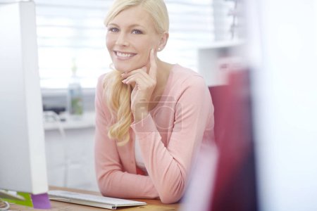 Foto de Es fácil cuando amas tu trabajo. Retrato de una atractiva joven empresaria sentada en un escritorio frente a una computadora que trabaja en su oficina. Una empleada sonriente que se siente positiva por su trabajo - Imagen libre de derechos
