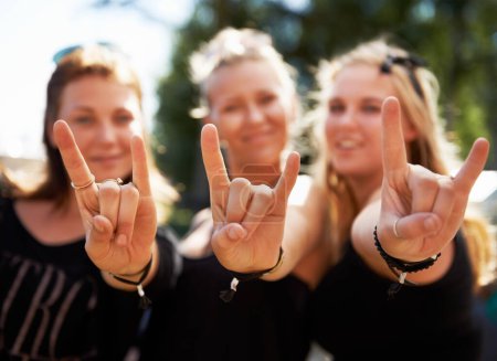 Photo for Keep on rocking. Three young girls giving you a rock and roll sign at a music festival - Royalty Free Image
