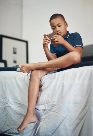 Foto de Jugar juegos educativos es realmente bueno para ellos. un niño usando un celular mientras está sentado en su cama - Imagen libre de derechos