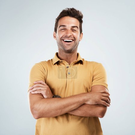 Foto de Te escucho. Retrato de un joven alegre sonriendo brillantemente con los brazos cruzados mientras está de pie sobre un fondo gris - Imagen libre de derechos