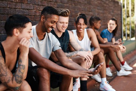 Photo for Just watch this...a group of sporty young people looking at something on a cellphone while sitting against a wall outdoors - Royalty Free Image