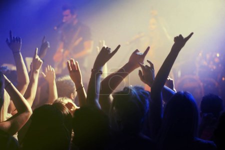 Hands in air, people dancing at concert or music festival with neon lights and energy at live event. Dance, fun and excited crowd of fans in arena for rock band, musician performance and spotlight