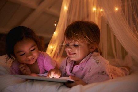 Téléchargez les photos : Nuit, lit et les filles avec une tablette, jeux et jouer pour le plaisir, le bonheur et se détendre ensemble. Enfants, enfants et jeunes femmes avec technologie, divertissement et gaieté avec un sourire ou une soirée. - en image libre de droit
