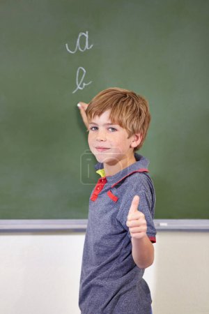 Photo for Portrait, child and student with thumbs up on blackboard in classroom, elementary school and mockup. Chalkboard, education and kid with hand gesture for like emoji, agreement and learning to write - Royalty Free Image