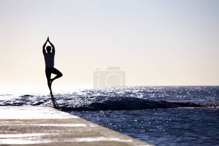 Téléchargez les photos : Homme, silhouette et yoga en méditation sur l'océan à la plage pour le bien-être spirituel, la paix intérieure ou l'espace de bien-être mental. Yogi mâle dans la pose de l'arbre pour l'équilibre, le corps sain ou la pleine conscience sur la maquette de la mer. - en image libre de droit