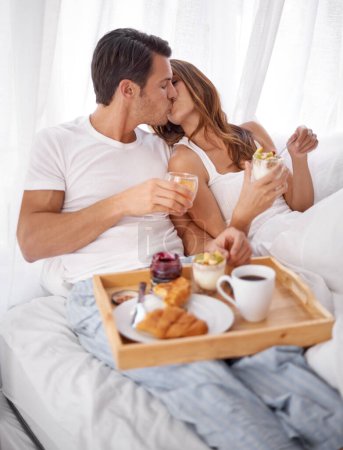 Foto de El desayuno en el dormitorio, el beso de amor y la pareja se relajan con la comida de la mañana, se unen y disfrutan de tiempo de calidad juntos en Toronto, Canadá. Romance matrimonial, servicio de habitaciones y personas en la cama del hotel para el Día de San Valentín. - Imagen libre de derechos