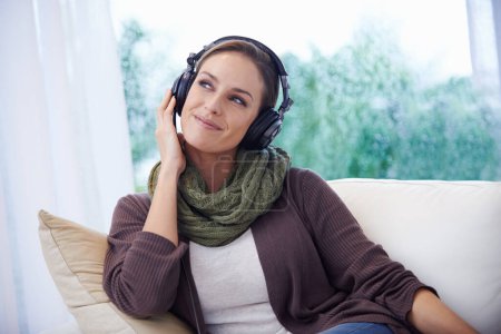 Photo for Experiencing the joys of music. A young woman sitting on the couch listening to music over her headphones - Royalty Free Image
