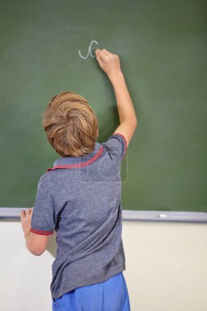 Téléchargez les photos : He knows the answer. A young boy writing on the blackboard at school - en image libre de droit