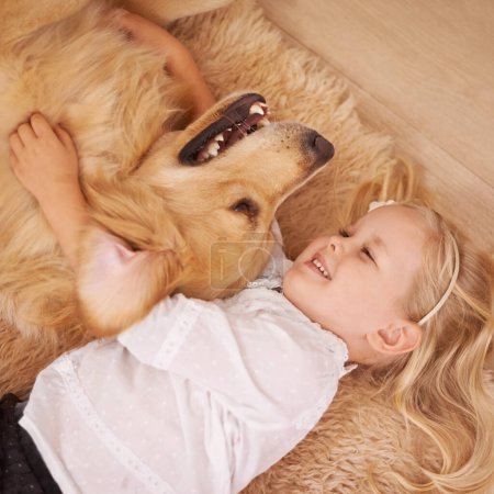 Photo for Dog, girl and hug together on floor in living room and golden retriever, kid and playing with pet on lounge carpet. Young child, labrador and happiness or family home, pets and children from above. - Royalty Free Image