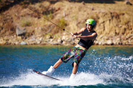 Téléchargez les photos : Splash, surf et wakeboard avec l'homme dans le lac pour les sports extrêmes, vacances d'été et de voyage. Vague, adrénaline junkie et fitness avec le gars ski sur la rivière pour la santé, l'aventure et la vitesse. - en image libre de droit