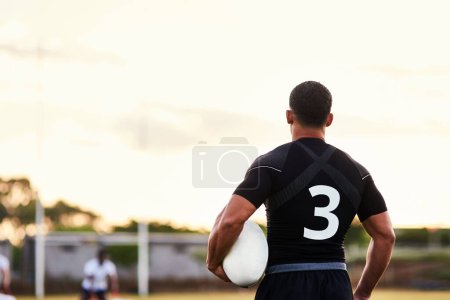 Téléchargez les photos : Va jusqu'au bout. un sportif méconnaissable debout seul et tenant une balle de rugby avant un entraînement matinal - en image libre de droit