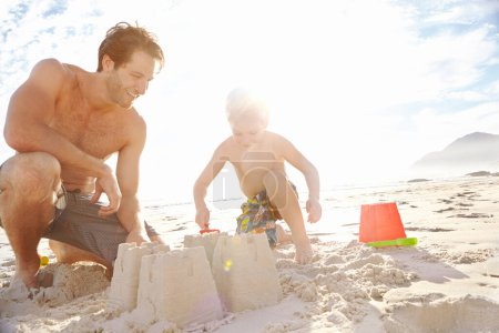 Téléchargez les photos : Papa et moi construisons un château de sable. un jeune père et son fils construisant un château de sable sur la plage - en image libre de droit