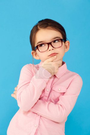 Photo for Thinking, ideas and girl with decision, choice and happiness against a blue studio background. Female child, kid and young person with glasses, thoughts and wonder with information, future and geek. - Royalty Free Image
