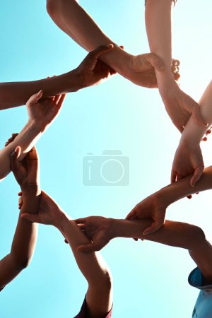 Photo pour Les mains, le lien et le cercle avec l'équipe et le ciel bleu avec un angle bas, la solidarité et la confiance avec la chaîne de bras et les gens ensemble. Travail d'équipe, motivation et lien avec la collaboration de groupe et la communauté. - image libre de droit