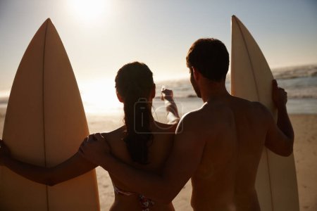 Téléchargez les photos : Frapper les vagues ensemble. Vue arrière d'un jeune couple de surfeurs regardant la plage et les vagues lointaines - en image libre de droit