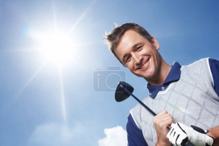 Téléchargez les photos : Allons faire du golf. Homme mûr souriant tenant son club de golf contre un ciel bleu - angle bas - en image libre de droit