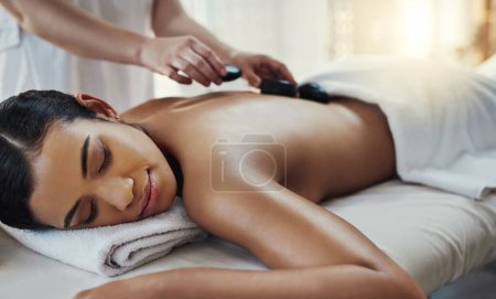 Photo for Woman, hands and sleeping for rock massage, skincare or relaxation on bed at indoor beauty spa. Hand of masseuse applying hot rocks to female in relax for physical therapy or back treatment at resort. - Royalty Free Image