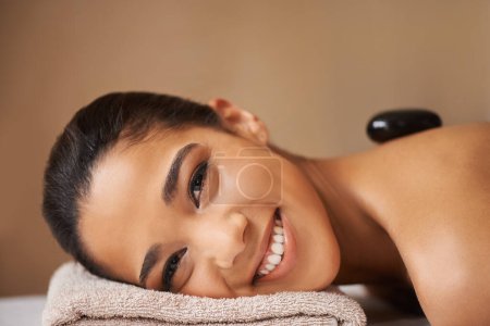 Photo for Portrait of happy woman, rock or back massage in spa to relax for zen, resting or wellness physical therapy. Face of girl smiling in salon to exfoliate for body healing treatment or hot stone therapy. - Royalty Free Image