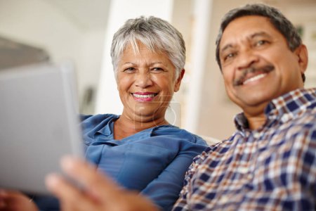 Foto de Abrazando los tiempos tecnológicos. una feliz pareja de ancianos usando una tableta digital juntos en casa - Imagen libre de derechos