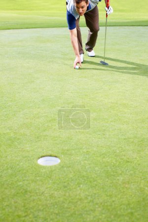 Foto de Golfista masculino colocando la pelota al putt. Hombre golfista colocando la pelota en la hierba y preparándose para putt - Imagen libre de derechos