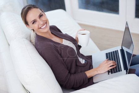 Foto de La vida doméstica moderna. Una joven sentada frente a su portátil sosteniendo una taza de café - Imagen libre de derechos