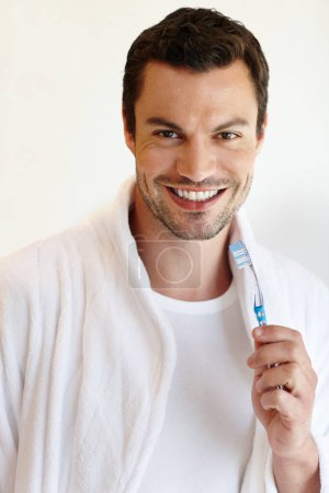 Photo for Dental care. A handsome man in a bathrobe smiling at the camera while he holds a toothbrush - Royalty Free Image