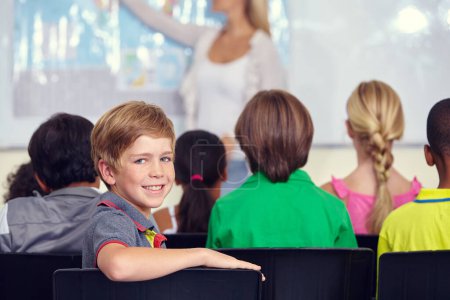 Téléchargez les photos : Il adore apprendre. Portrait d'un petit garçon assis avec ses camarades de classe pendant une leçon - en image libre de droit
