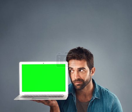Photo for Man, laptop and thinking on mockup green screen for advertising or marketing against a grey studio background. Thoughtful male person showing computer display, mock up or copy space for advertisement. - Royalty Free Image