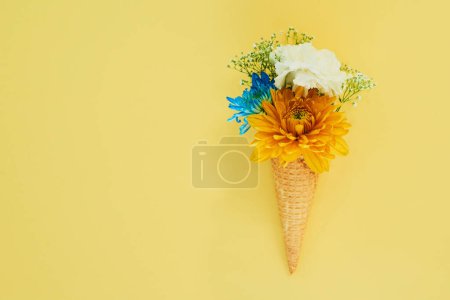 Téléchargez les photos : Crème glacée aux fleurs dans un cône en studio pour la création, l'art ou la décoration avec bouquet frais et coloré. Créativité, nature morte et plantes florales dans un dessert isolé par fond jaune avec maquette - en image libre de droit