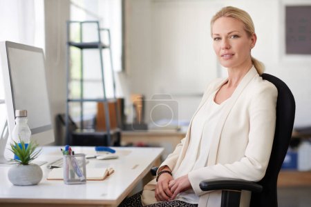 Photo for Feeling good about my career choices. Relaxed businesswoman looking positively at the camera in her bright office space - Royalty Free Image