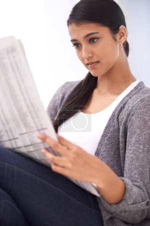 Photo for Sunday morning ritual. A beautiful young woman reading the newspaper in her lounge - Royalty Free Image