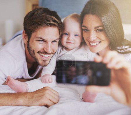 Photo for Happy family, parents and selfie of baby on bed in home for love, care and quality time together. Mother, father and newborn child smile for photograph, fun memory and happiness of bonding in bedroom. - Royalty Free Image