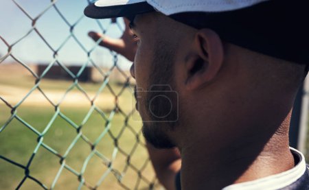 Téléchargez les photos : S'il ne la joue pas, il la regarde. un jeune homme regardant un match de baseball derrière la clôture - en image libre de droit