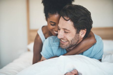 Photo for Happy couple, bed and smile in hug for morning, relax or bonding relationship at home. Interracial man and woman smiling and hugging in joyful happiness for relaxing weekend together in the bedroom. - Royalty Free Image