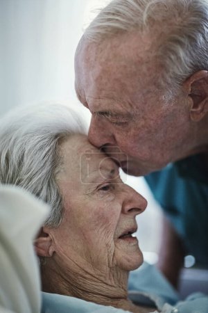 Téléchargez les photos : Senior, baiser et couple à l'hôpital pour l'amour, visite malade malade malade et l'espoir de guérison. Clinique, homme et femme âgés baisers sur le front pour l'empathie, la gentillesse et le soutien aux soins de santé - en image libre de droit