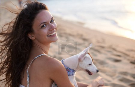Téléchargez les photos : On adore la plage. une jolie jeune femme profitant de la plage avec son chien - en image libre de droit