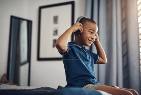 Foto de Las canciones optimistas ayudan a mantener un estado de ánimo positivo. un chico joven escuchando música a través de auriculares mientras está sentado en casa - Imagen libre de derechos
