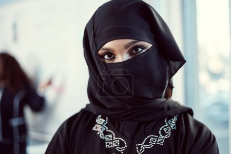 Photo for Im making my mark in the business world. Cropped portrait of an attractive young arabic businesswoman standing with her arms crossed in the office with her colleagues in the background - Royalty Free Image