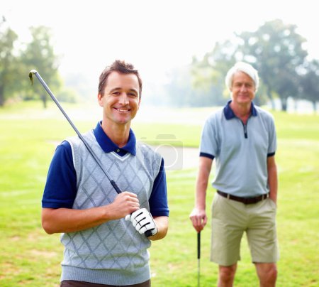 Téléchargez les photos : Un golfeur intelligent souriant. Portrait d'un homme intelligent tenant un club de golf et souriant avec son père debout en arrière-plan - en image libre de droit