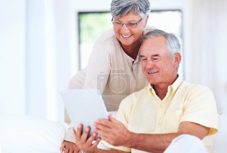Foto de Pareja usando tableta digital en casa. Alegre pareja madura sonriendo mientras usa la tableta digital en casa - Imagen libre de derechos
