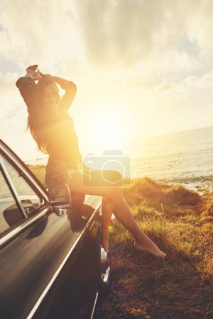 Photo for Road trip, portrait and sunset with a woman at the coast, sitting on her car bonnet during travel for freedom or escape. Nature, lens flare and water with a young female tourist traveling in summer. - Royalty Free Image