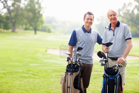 Foto de Padre e hijo sonriendo en el campo de golf. Retrato de padre e hijo de pie con bolsas de golf y sonriente - Imagen libre de derechos